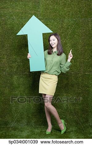 Stock Photo - A woman standing with a green arrow. Fotosearch