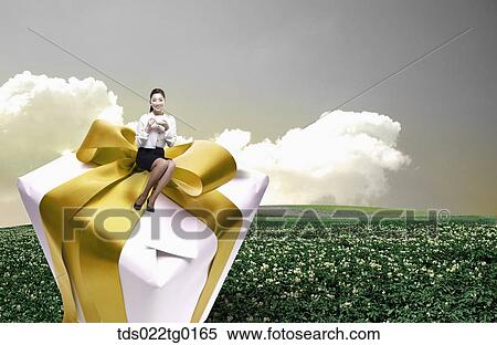 Stock Photography - business woman is sitting on the gift box with coffee. Fotosearch