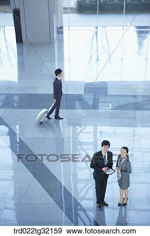 Stock Photo - Businessmen standing with suitcase and having a talk. Fotosearch
