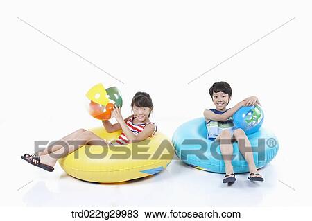 Stock Image - children holding beach balls and sitting on the tubes. Fotosearch