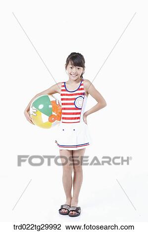 Stock Image - girl is standing with holding beach ball in her arm. Fotosearch