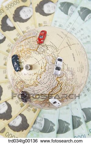 Stock Photograph - miniature cars on the globe and spreaded money bills. Fotosearch
