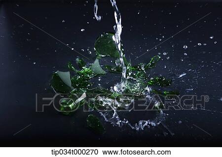Stock Image - Pouring water onto the broken glass bottle. Fotosearch
