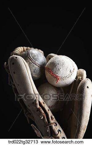 Stock Image - Worn out baseballs in a glove. Fotosearch