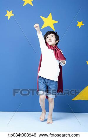 Stock Photograph - a boy posing like a superman with a red cape around his neck in blue background with stars. Fotosearch