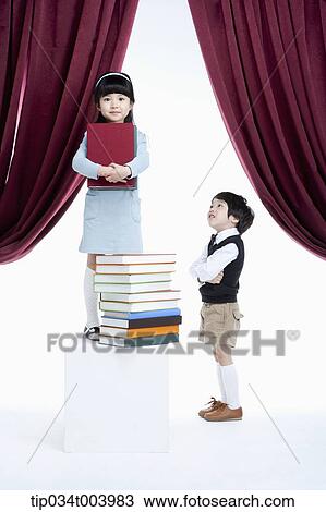 Stock Image - a boy standing next to a girl with pile of books on a stage. Fotosearch