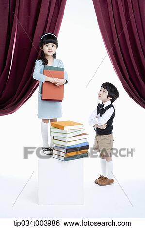 Stock Photograph - a boy standing next to a girl with pile of books on a stage. Fotosearch