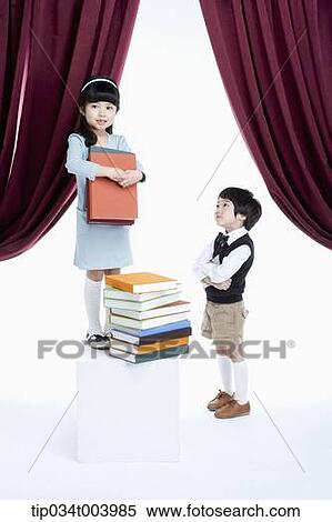 Stock Photography - a boy standing next to a girl with pile of books on a stage. Fotosearch