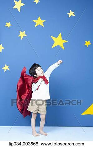 Stock Photography - a boy wearing a red cape posing like a superman in front of a blue wall full of stars. Fotosearch