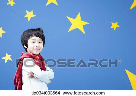 Picture - a boy wearing a red cape standing with arms crossed in front of a blue wall full of stars. Fotosearch