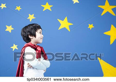 Stock Image - a boy wearing a red cape standing with arms crossed in front of a blue wall full of stars. Fotosearch