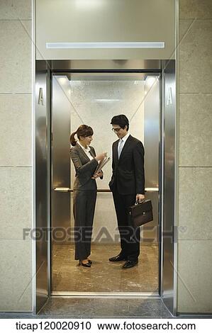 Stock Image - a businessman and woman discussing in elevator. Fotosearch