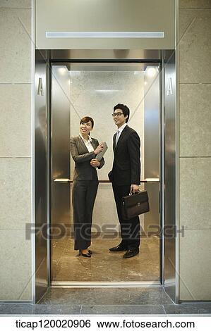 Stock Photograph - a businessman and woman looking at the floor numbers in elevator. Fotosearch