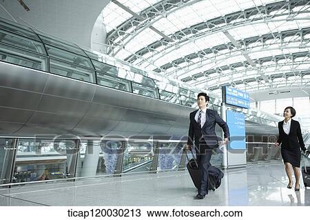 Stock Image - a businessman and woman walking fast in Incheon airport. Fotosearch