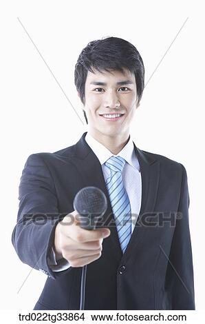 Picture - a businessman in a black suit handing a microphone to camera . Fotosearch