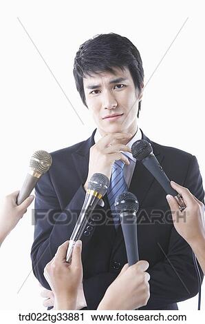 Stock Image - a businessman in a black suit in conference meeting with many microphones . Fotosearch