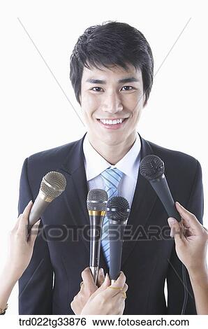 Stock Photograph - a businessman in a black suit in conference meeting with many microphones . Fotosearch