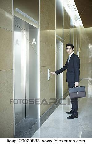 Stock Image - a businessman pressing button for an elevator in a office building. Fotosearch