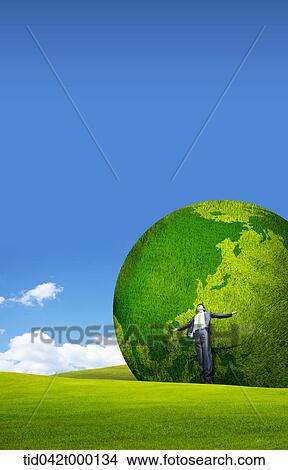 Picture - a businessman standing in front of a huge green globe . Fotosearch