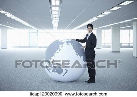 a businessman standing next to a huge globe in an empty room View Large Photo Image Stock Image - a businessman standing next to a huge globe in an empty room. Fotosearch