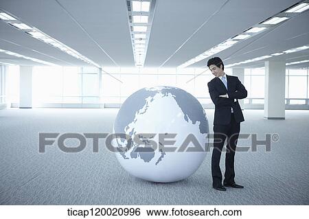 a businessman standing with arms crossed next a huge globe in an empty room View Large Photo Image Stock Photograph - a businessman standing with arms crossed next a huge globe in an empty room. Fotosearch