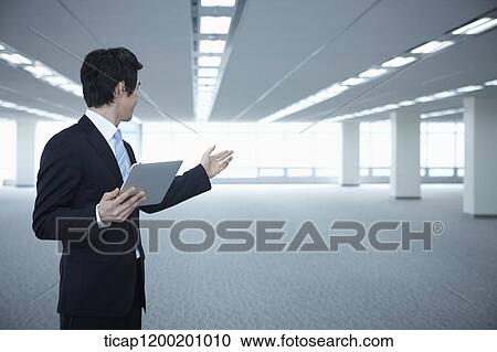 a businessman standing with tablet PC showing an empty room View Large Photo Image Stock Image - a businessman standing with tablet PC showing an empty room. Fotosearch