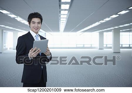 Stock Photo - a businessman standing with tablet PC in an empty room. Fotosearch