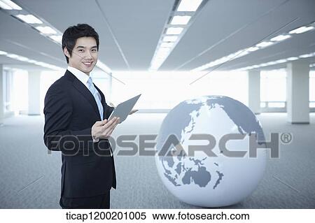 a businessman standing with tablet PC next to a globe in an empty room View Large Photo Image Stock Photography - a businessman standing with tablet PC next to a globe in an empty room. Fotosearch