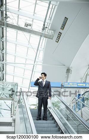 Stock Image - a businessman talking on the phone in escalator of Incheon airport. Fotosearch