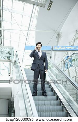 Stock Photography - a businessman talking on the phone in escalator of Incheon airport. Fotosearch