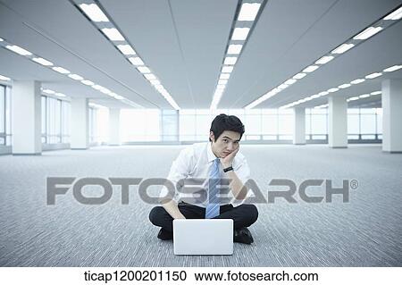 a businessman using laptop on the floor of an empty room with a hand on his chin View Large Photo Image Stock Image - a businessman using laptop on the floor of an empty room with a hand on his chin. Fotosearch