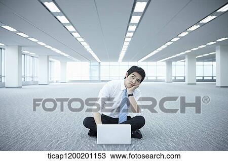 a businessman using laptop on the floor of an empty room with a hand on his chin View Large Photo Image Stock Image - a businessman using laptop on the floor of an empty room with a hand on his chin. Fotosearch