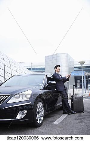 a businessman with a luggage leaning on a car using a tablet PC View Large Photo Image Stock Photograph - a businessman with a luggage leaning on a car using a tablet PC. Fotosearch