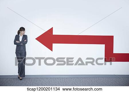 a businesswoman looking at an arrow on the wall while leaning on the wall View Large Photo Image Picture - a businesswoman looking at an arrow on the wall while leaning on the wall. Fotosearch