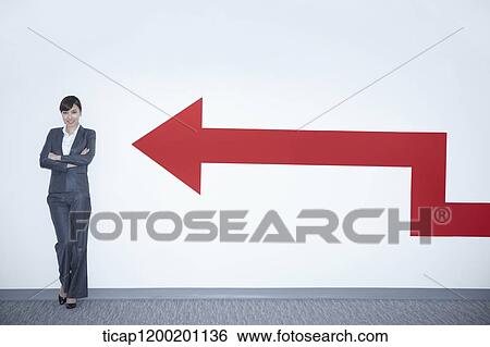 a businesswoman standing with arms crossed next to a wall with an arrow View Large Photo Image Stock Photograph - a businesswoman standing with arms crossed next to a wall with an arrow. Fotosearch