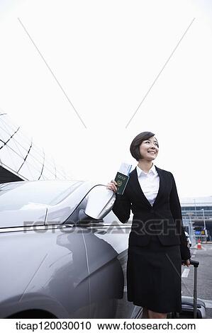Stock Image - a businesswoman with a luggage and a passport standing next to a car. Fotosearch