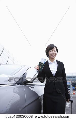 Stock Photo - a businesswoman with a luggage and a passport standing next to a car. Fotosearch