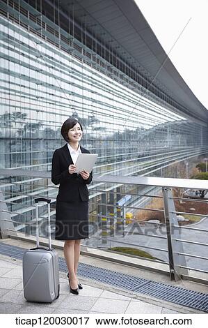 Stock Photo - a businesswoman with a luggage and a tabletPC standing in Incheon airport. Fotosearch