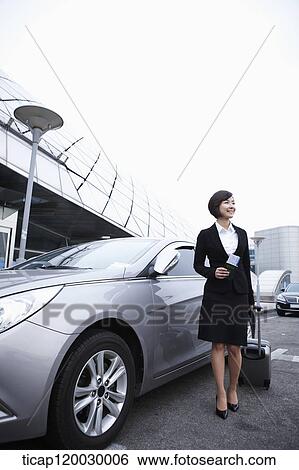 Stock Photograph - a businesswoman with a luggage standing next to a car. Fotosearch