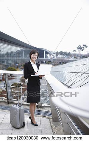 Stock Image - a businesswoman with a luggage working on laptop in Incheon airport. Fotosearch
