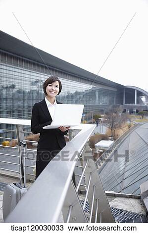 Stock Image - a businesswoman with a luggage working on laptop in Incheon airport. Fotosearch