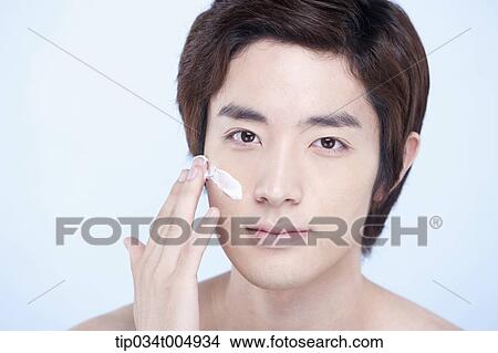 Picture - a close up shot of a topless man putting on white cream lotion. Fotosearch