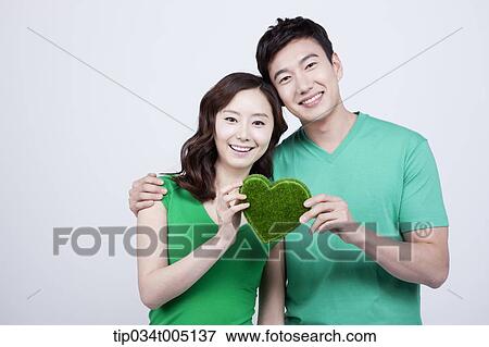 Stock Photo - a couple in green t-shirts holding a heart shape figure made from grass. Fotosearch