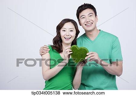 Stock Photo - a couple in green t-shirts holding a heart shape figure made from grass. Fotosearch