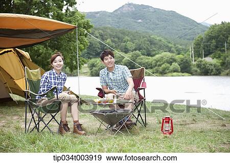 a couple sitting on camping chairs smiling at camera while having a camping meal View Large Photo Image Stock Photo - a couple sitting on camping chairs smiling at camera while having a camping meal. Fotosearch