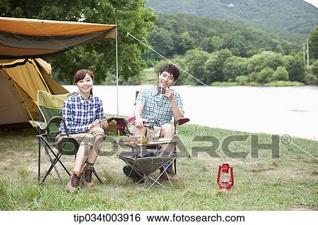 Stock Photograph - a couple sitting on camping chairs having a camping meal. Fotosearch