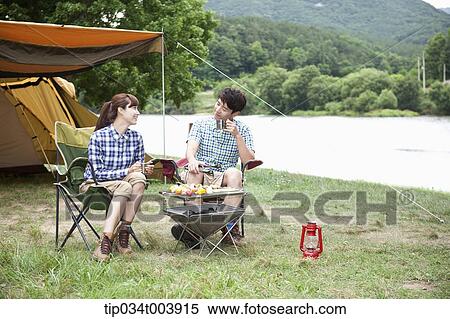 a couple sitting on camping chairs chatting while having a camping meal View Large Photo Image Stock Photography - a couple sitting on camping chairs chatting while having a camping meal. Fotosearch