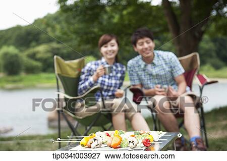 a couple sitting on camping chairs with a grill in front of them View Large Photo Image Stock Photo - a couple sitting on camping chairs with a grill in front of them . Fotosearch