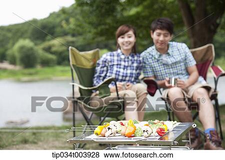 a couple sitting on camping chairs with a grill in front of them View Large Photo Image Stock Photo - a couple sitting on camping chairs with a grill in front of them . Fotosearch