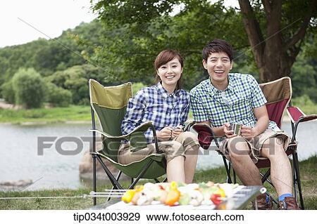 a couple sitting on camping chairs with a grill in front of them View Large Photo Image Stock Photo - a couple sitting on camping chairs with a grill in front of them . Fotosearch